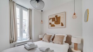 Un letto rifatto con asciugamani piegati, un quadro astratto di grandi dimensioni e una lampada moderna.