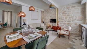 Un soggiorno moderno con una parete in pietra, un'area pranzo con un tavolo in legno apparecchiato per quattro persone e un angolo cottura con lavatrice.