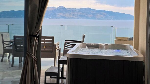 Ein Balkon mit Whirlpool, Stühlen und Blick auf Berge und Wasser.