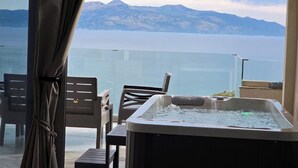 Ein Balkon mit Whirlpool, Stühlen und Blick auf Berge und Wasser.
