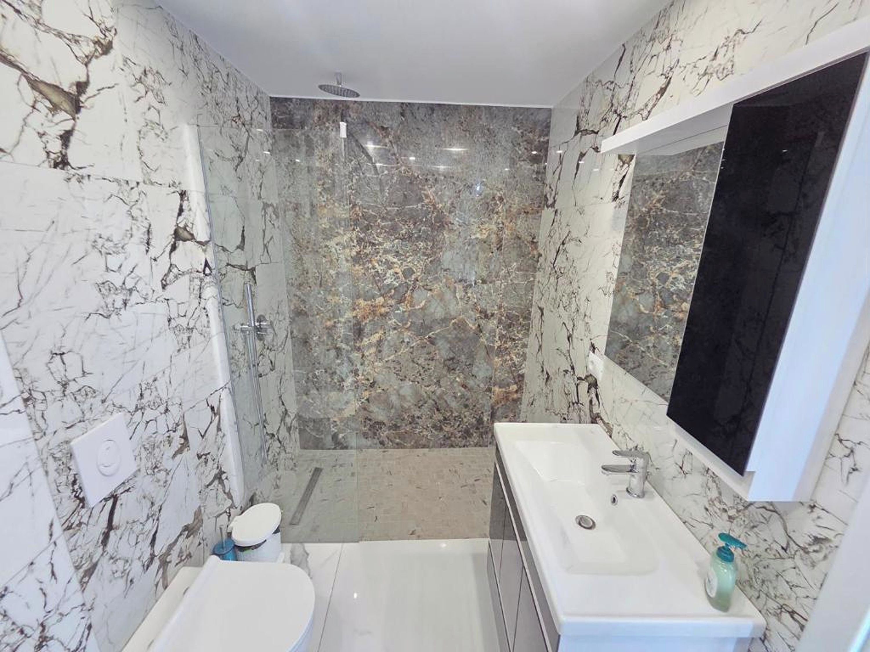 Un bagno con parete in marmo, un water, una vasca e un lavabo.