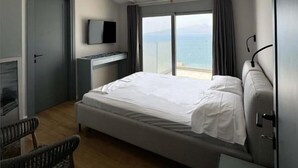 Ein Hotelzimmer mit Bett, Fernseher, Schreibtisch, Stuhl und Blick auf das Meer.