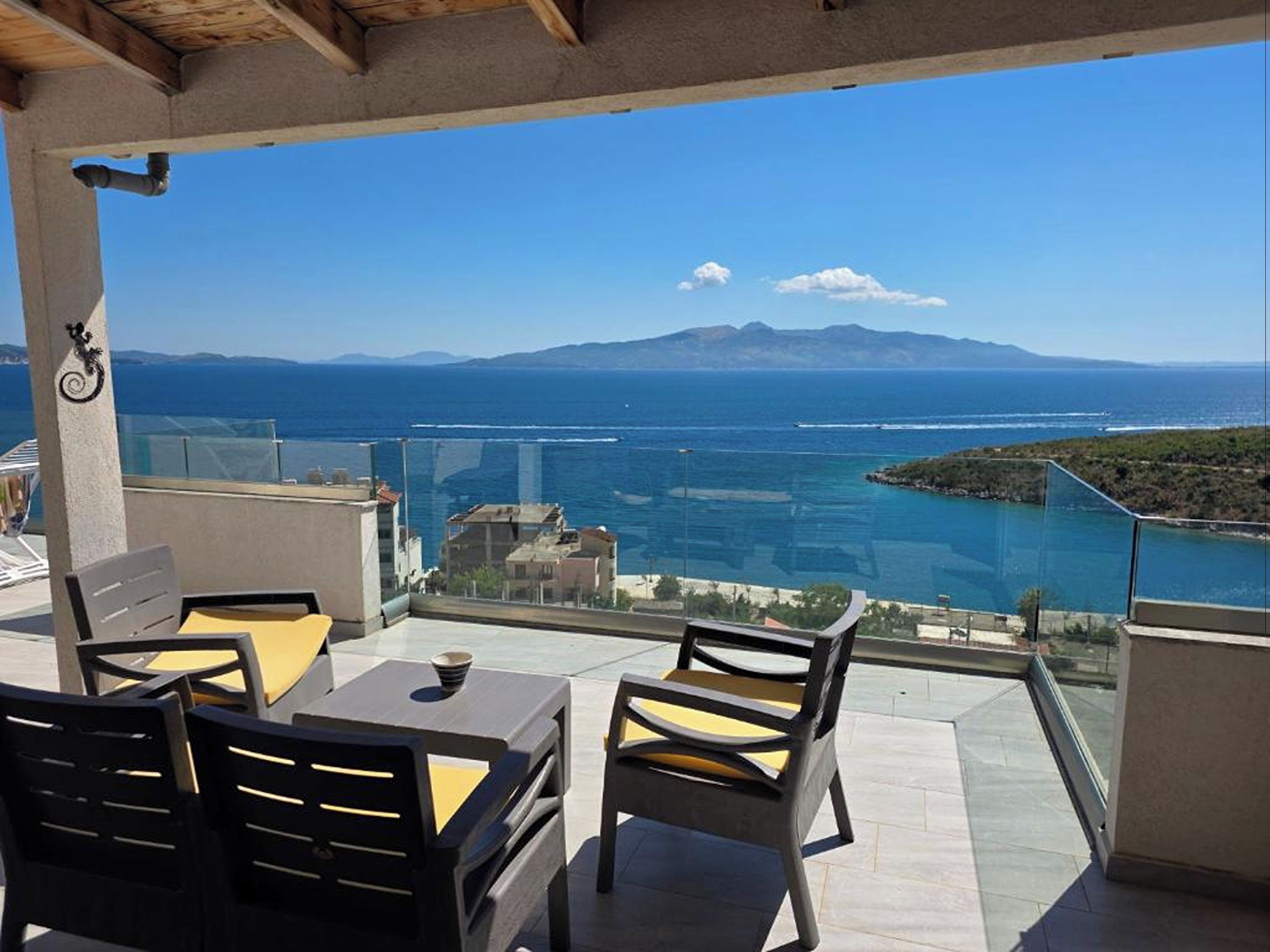 Een balkon met een tafel en stoelen, uitkijkend op een kustgezicht met bergen in de verte.
