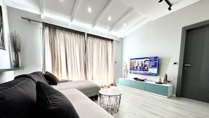 Ein modernes Wohnzimmer mit einer Couch, einem runden Couchtisch, einem Fernseher auf einem Schrank und einer Tür.