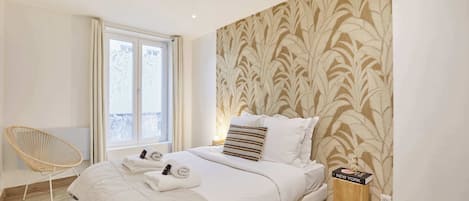 A bedroom with a bed, a chair, a window, and a wall with a leaf pattern.