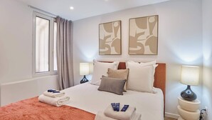 Hotelkamer met een bed, twee abstracte schilderijen aan de muur, een raam met gordijnen, een nachtkastje met een lamp en handdoeken op het bed.