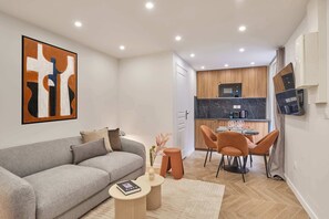 Ein modernes Wohnzimmer mit einem grauen Sofa, einem Couchtisch und einem Essbereich mit orangefarbenen Stühlen.