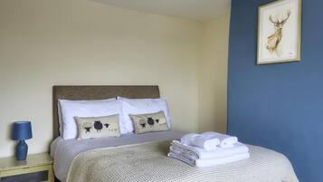 Una cama bien hecha con almohadas, una toalla doblada, una lámpara y un cuadro en la pared.
