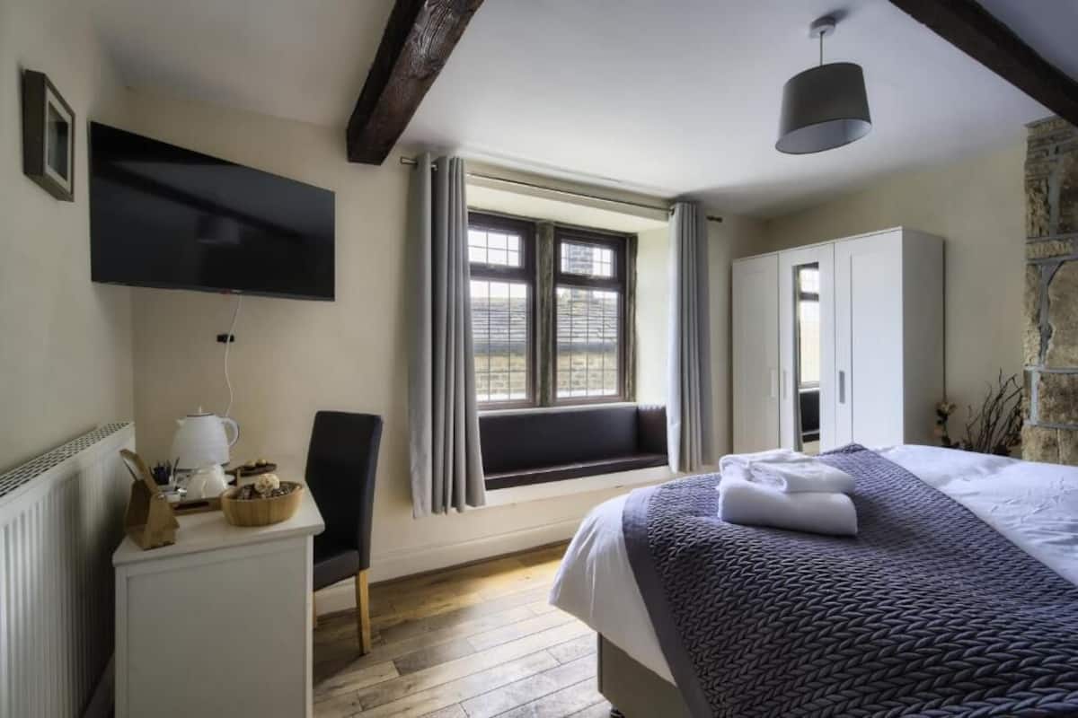 Une chambre à coucher comprenant un lit, un bureau, une chaise, une fenêtre avec des rideaux, un téléviseur et une armoire.