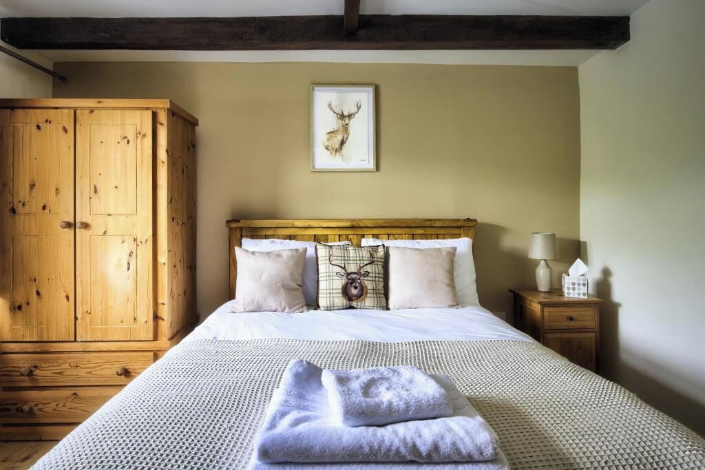 A bedroom with a wooden wardrobe, a bed with white bedding, a framed deer head artwork on the wall, and a bedside table with a lamp and tissues.