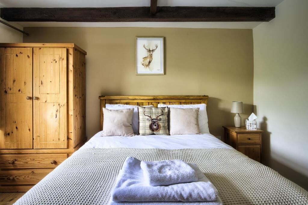 A bedroom with a wooden wardrobe, a bed with white bedding, a framed deer head artwork, and a bedside table with a lamp and tissues.