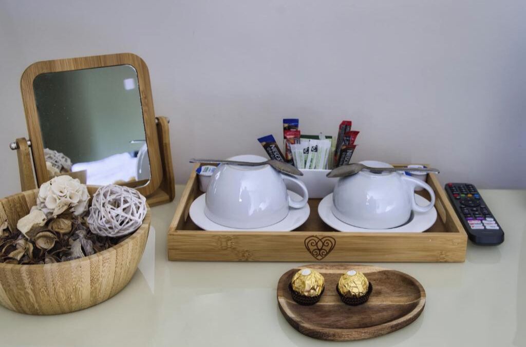 A tray with white cups and saucers, a remote control, and two chocolate truffles on a wooden tray.