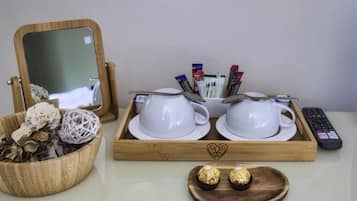 Una bandeja de madera con tazas y platillos blancos, un control remoto y dos bombones de chocolate.