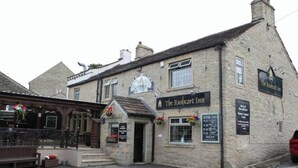 El Rushcart Inn, un edificio de piedra con un letrero de pub tradicional, una entrada pequeña y cestas de flores.