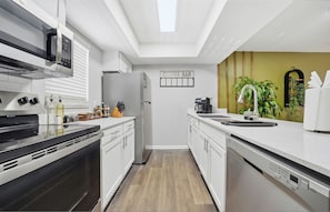A modern kitchen with a coffee bar, stainless steel appliances, and a wooden floor. - Modern 2BR/2BA w/ King Bed, Pool + Gym #10 (Tampa)