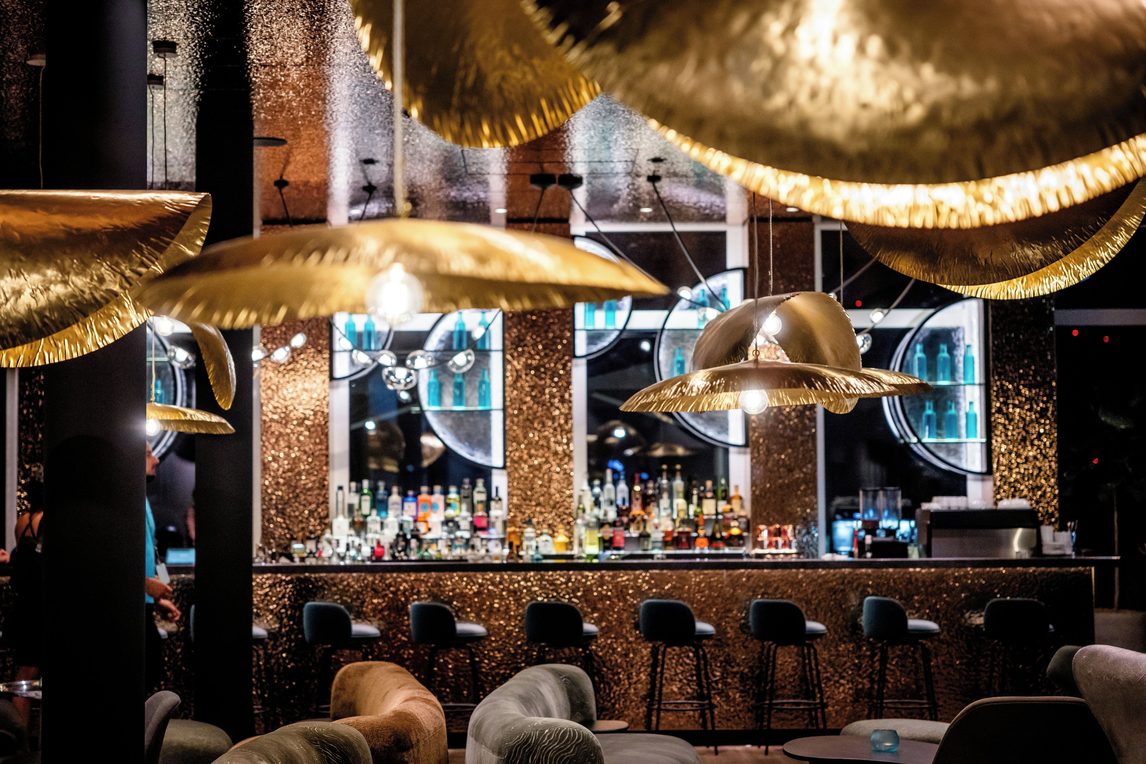 Eine Bar mit mehreren Pendelleuchten, einer Theke voller Flaschen und Sitzgelegenheiten mit Barhocker.