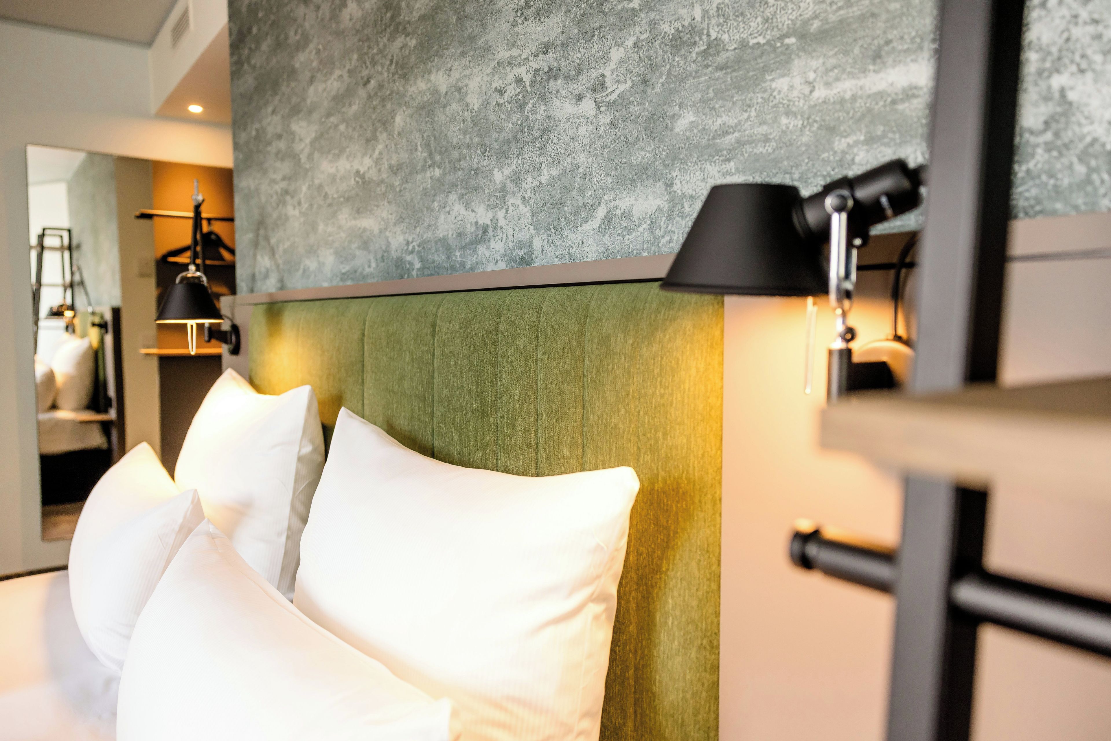 A hotel room with a bed, pillows, a headboard, a lamp, and a textured wall.