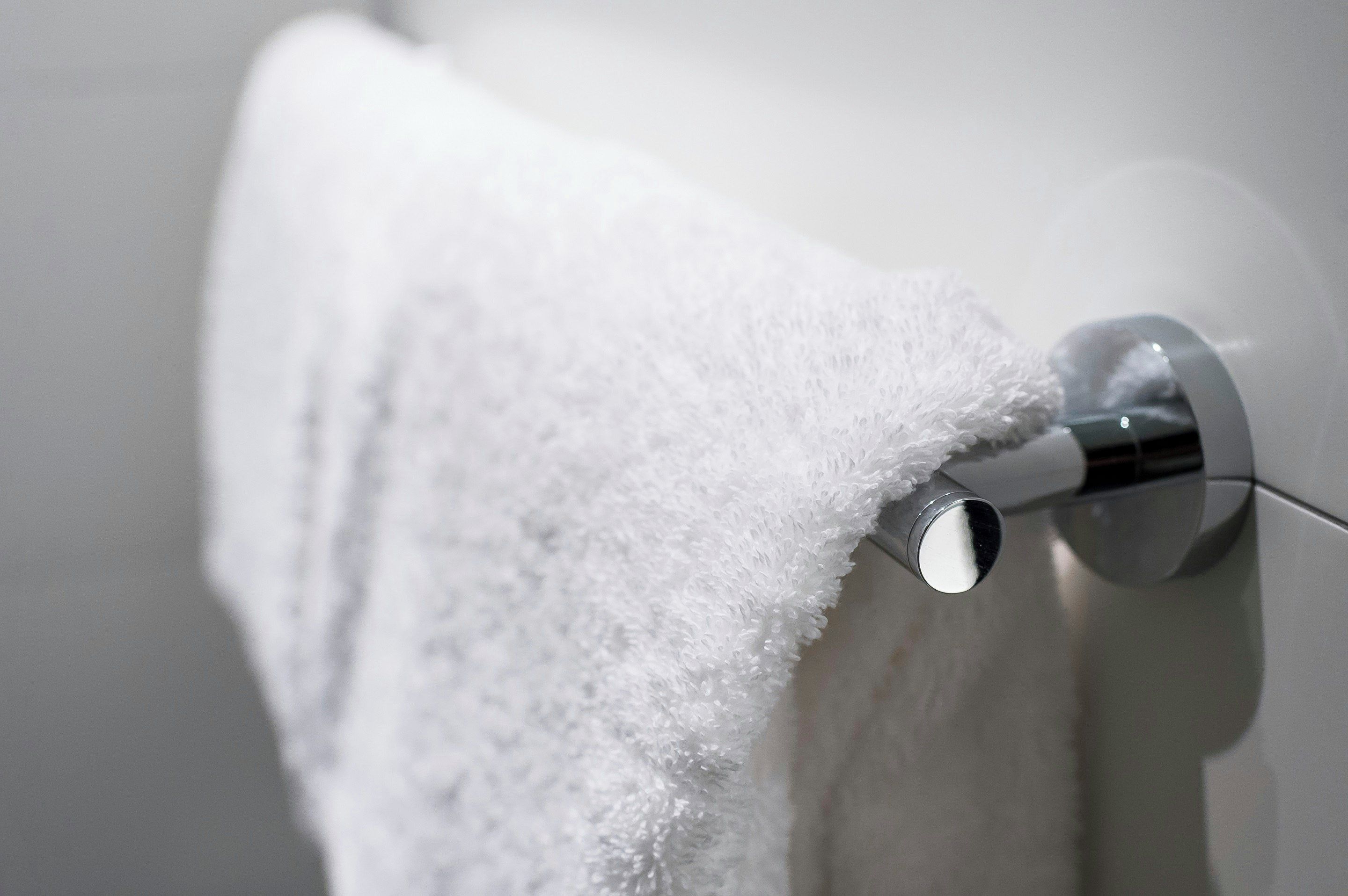 A white towel hanging on a metallic towel bar in a bathroom.