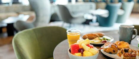 A breakfast setting with a bowl of fruit, croissants, and a mug on a round table.