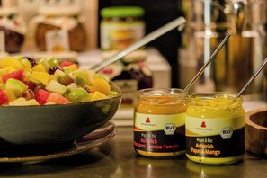 Un cuenco de ensalada de frutas y dos frascos de condimentos veganos y orgánicos sobre una encimera de cocina.
