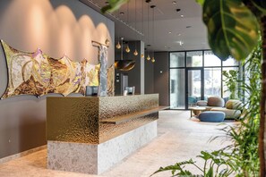 Un área de recepción de diseño moderno, con un mostrador texturizado, una gran obra de arte abstracta en la pared y una zona de estar con vistas amplias a través de grandes ventanales.
