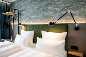 Habitación de hotel con una cama, dos lámparas de noche, un cabecero verde y una pared con textura.