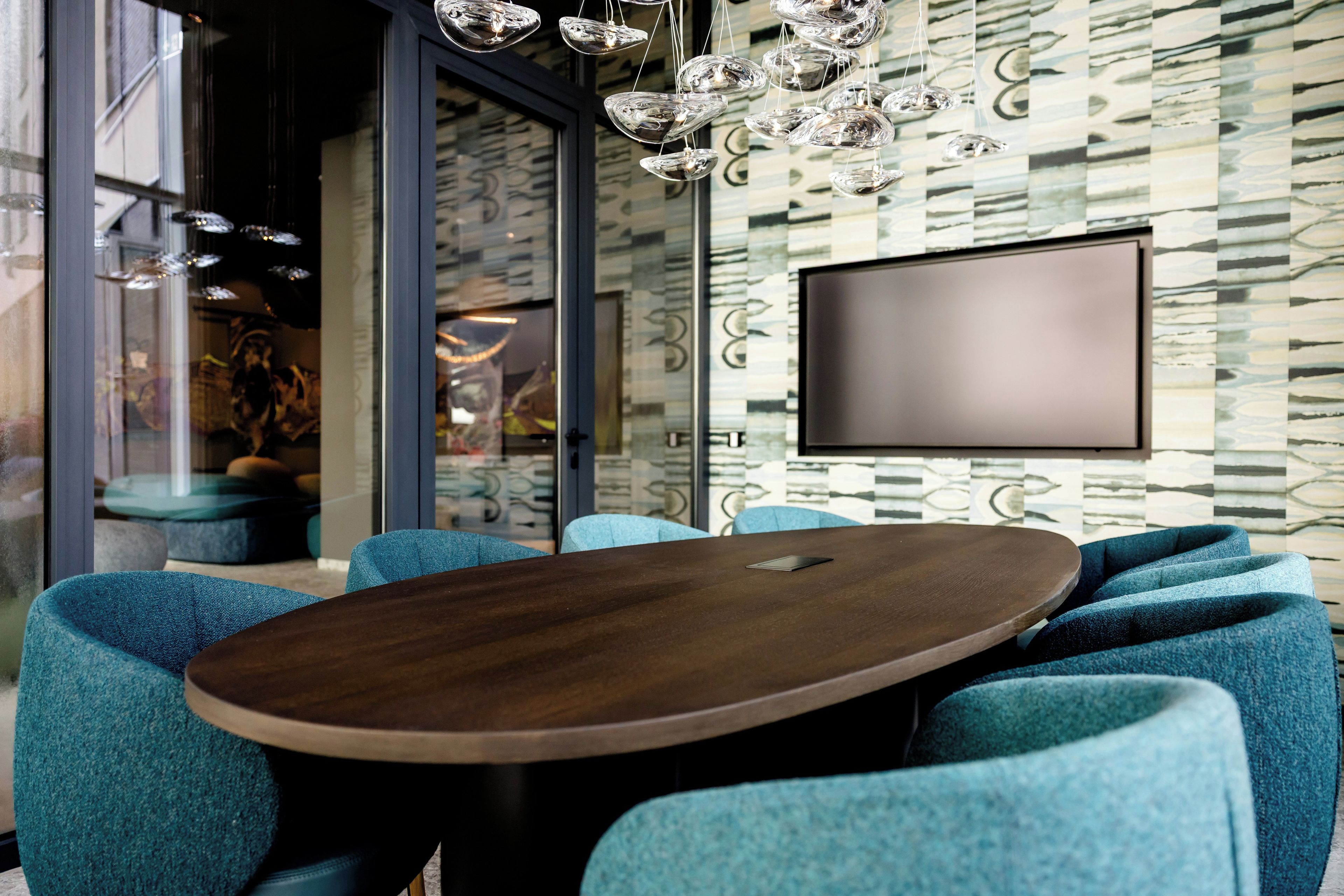 Una sala de conferencias moderna con una mesa de madera, sillas tapizadas en azul, un televisor de pantalla plana grande y un papel tapiz estampado.