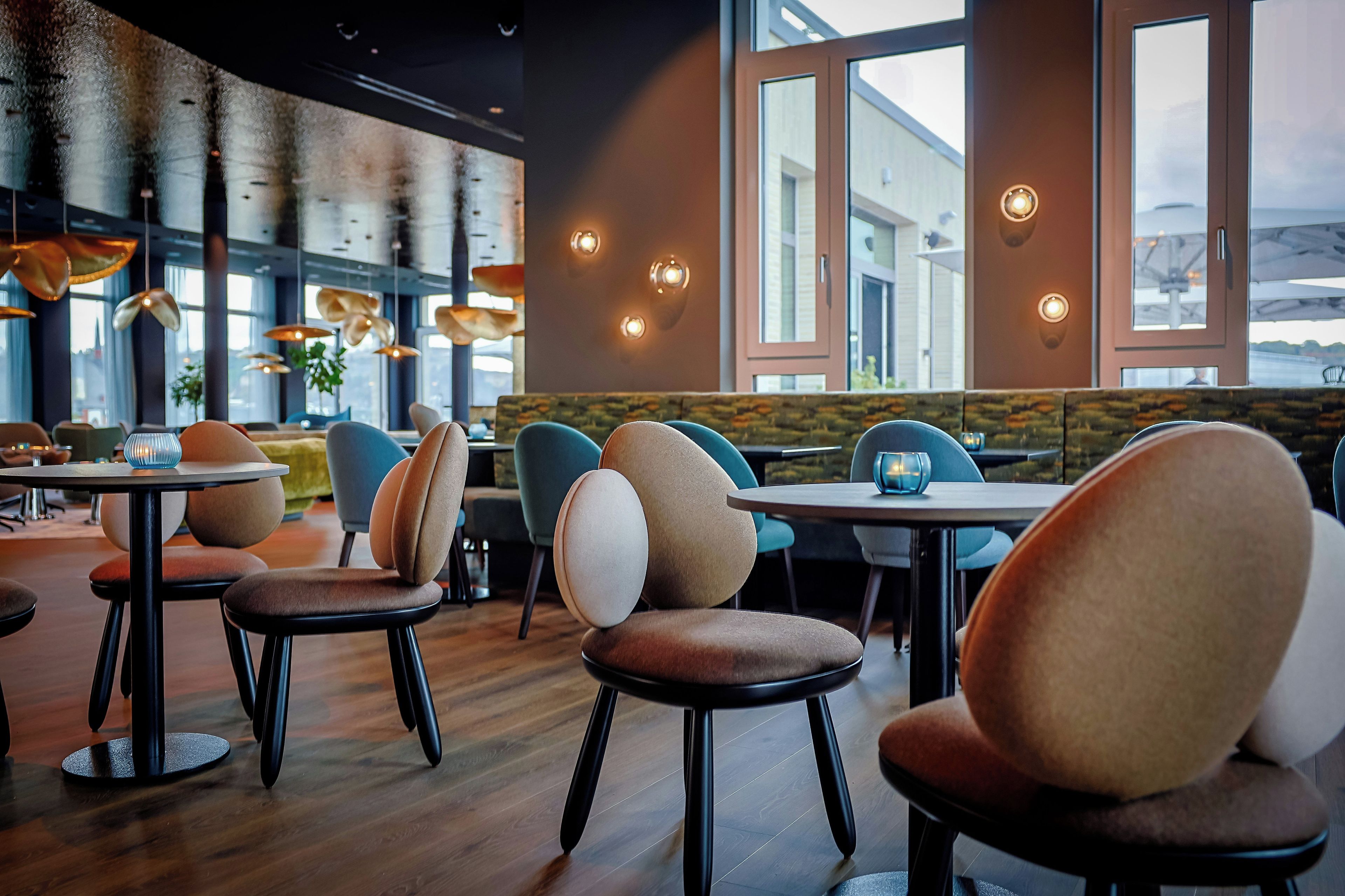 A modern restaurant interior with round tables, cushioned chairs, and pendant lighting.