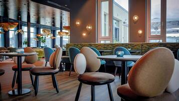 A modern restaurant interior with round tables, cushioned chairs, and pendant lighting.