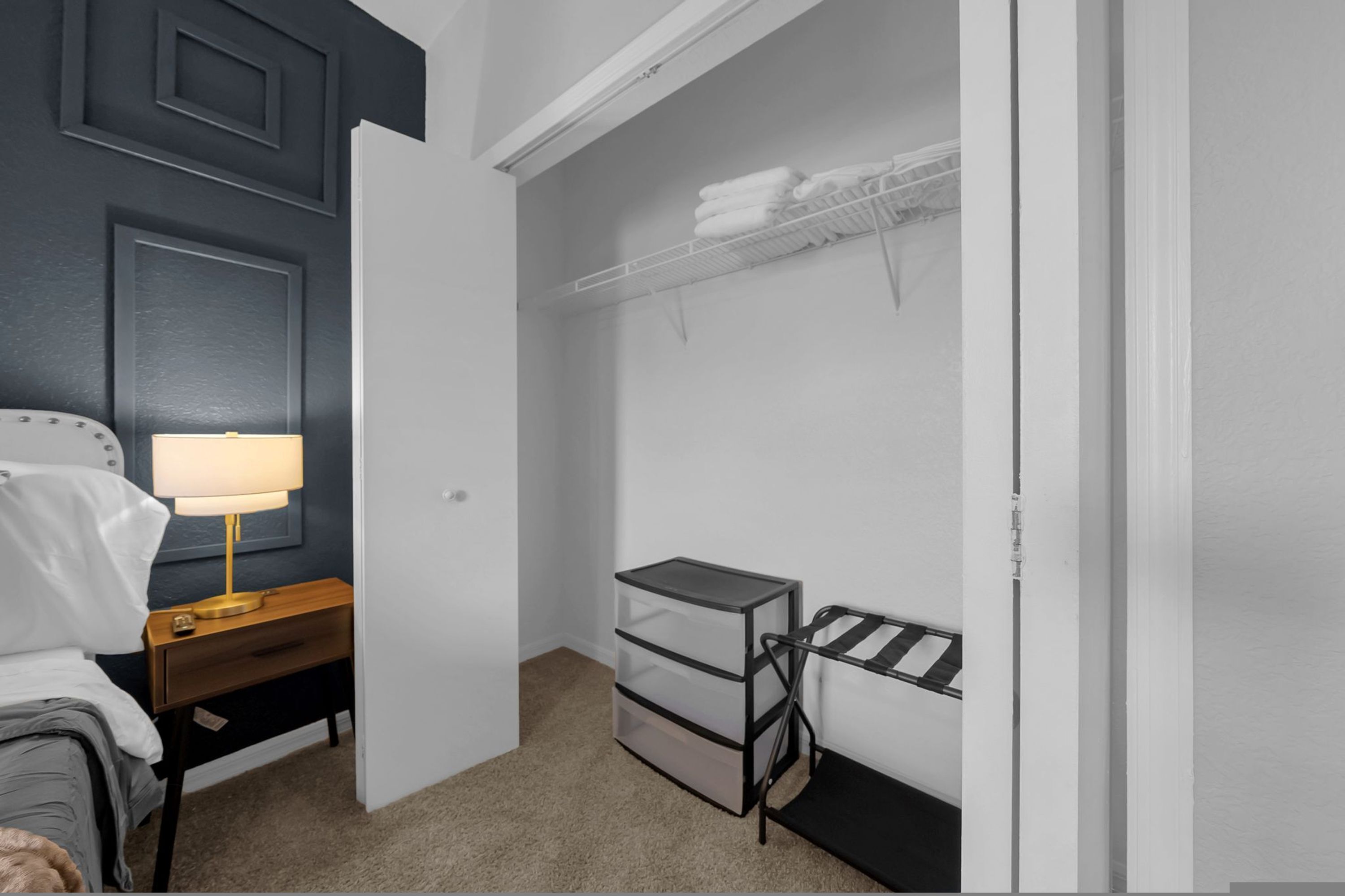 Une chambre à coucher comprenant un lit, une lampe de chevet, une commode et un placard avec des étagères et des tiroirs.