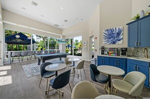 Un espace piscine avec des chaises longues et une table de billard, un bar avec un coin café, et une vue sur la verdure environnante.