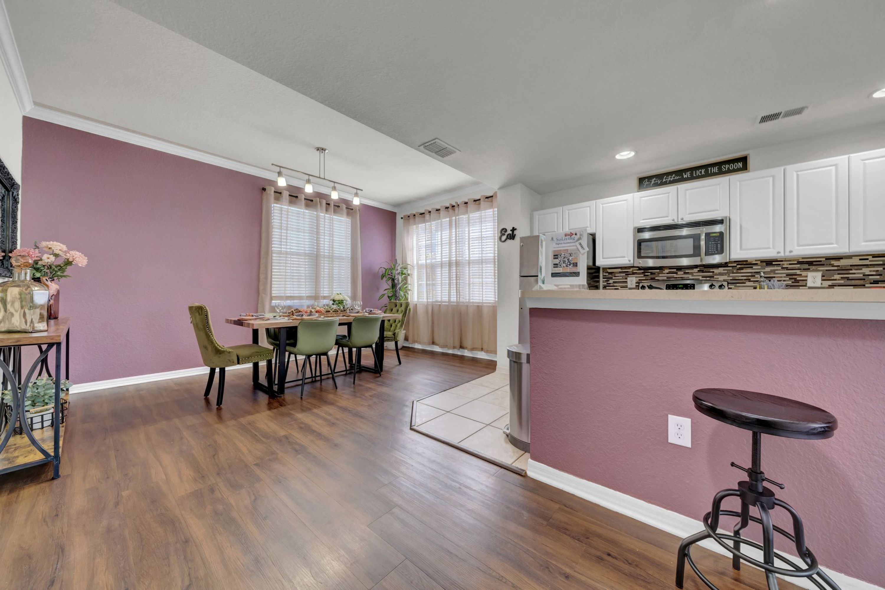 A modern kitchen with white cabinets, a stainless steel microwave, and a dining area with a table and chairs.