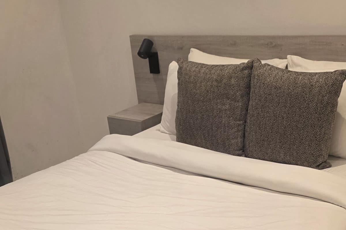 A neatly made bed with a rolled towel, a headboard, and a nightstand with a lamp.