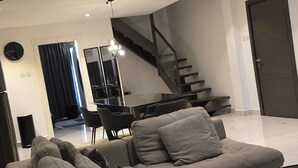 A modern living room with a sectional sofa, a dining area, a staircase, and a glass railing. - ebs properties ghana (Accra)