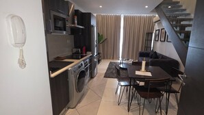 A modern kitchen with a washing machine, a dining area with a table and chairs, and a staircase. - ebs properties ghana (Accra)
