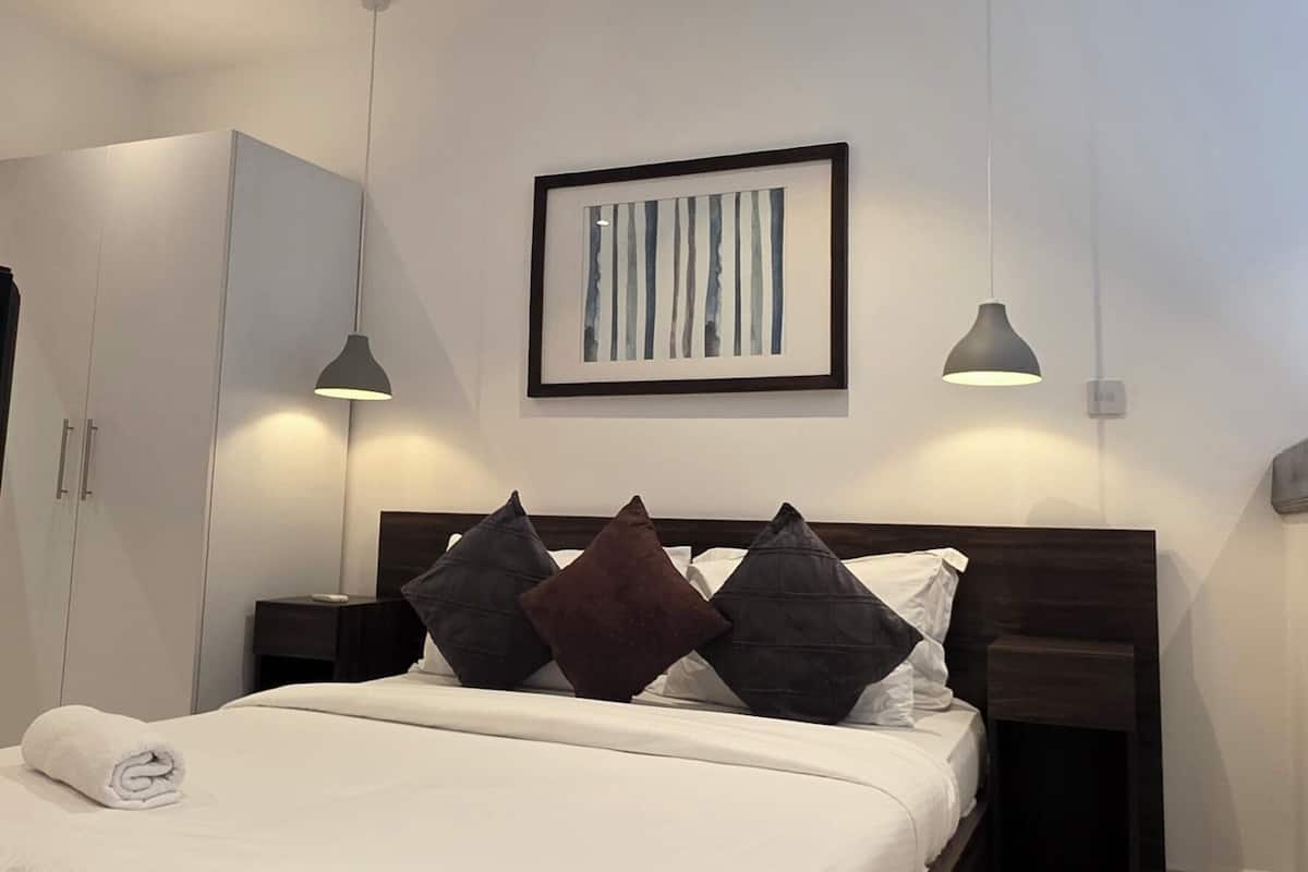 A modern bedroom with a large bed, bedside tables, a framed artwork, and pendant lighting.