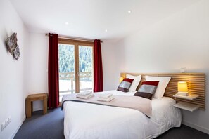 A bedroom with a bed, bedside table, and a window with curtains. - Chalet in Vanoise With Spa and Stunning Views (Peisey-Nancroix)