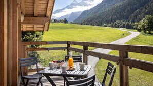 Una terraza de madera con una mesa dispuesta para el desayuno, con vistas a un paisaje montañoso.
