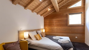 Un dormitorio con techo de madera, una cama con almohadas, una mesita de noche con una lámpara y una ventana.