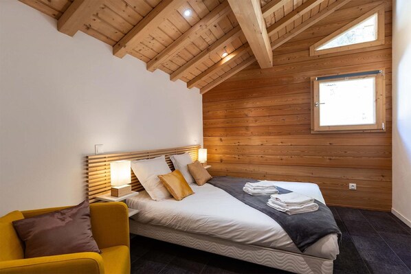 A bedroom with a wooden ceiling, a bed with pillows, a bedside table with a lamp, and a window. - Chalet in Vanoise With Spa and Stunning Views (Peisey-Nancroix)