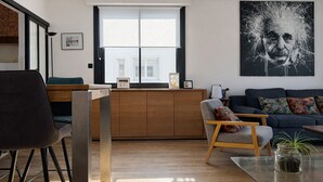 En moderne stue med et træskab, en sofa, en lænestol og et stort vindue.