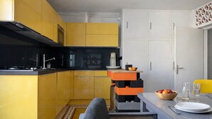 Et lille køkken med gule skabe, en sort komfur og et spiseområde med et bord dækket til to.