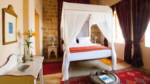 A four-poster bed with a white canopy, a red throw blanket, a small bedside table with a lamp, and a red patterned rug. - Vivila in the medieval city of Rhodes (Rodos)