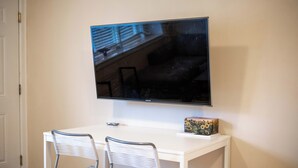 Un bureau blanc avec deux chaises, un téléviseur à écran plat fixé au mur au-dessus, et une petite boîte décorative posée sur le bureau.