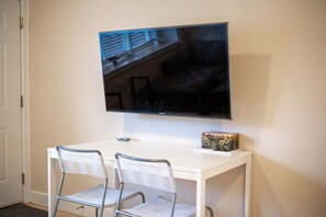 Un bureau blanc avec deux chaises, un téléviseur à écran plat fixé au mur au-dessus, et une petite boîte décorative posée sur le bureau.