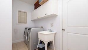 Une buanderie équipée d’un lave-linge, d’un évier, d’une poubelle et d’une porte blanche.