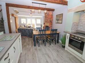 A modern kitchen with a dining area, wooden beams, and a brick wall. - Milburn Cottage (Keighley)
