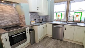 Een moderne keuken met witte kasten, een RVS vaatwasser, een inbouwoven en een raam met een groen glas-in-lood ontwerp.
