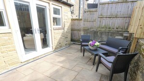 Een terras met stenen vloer, een zithoek met een tafel en stoelen, en een schuifdeur die naar een kamer leidt.