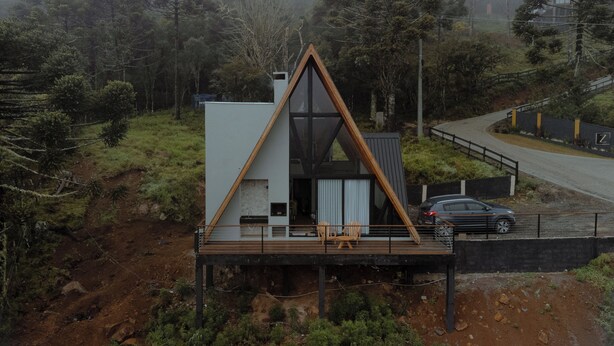 Une maison moderne avec un toit triangulaire, une terrasse avec des chaises et une voiture garée à proximité.